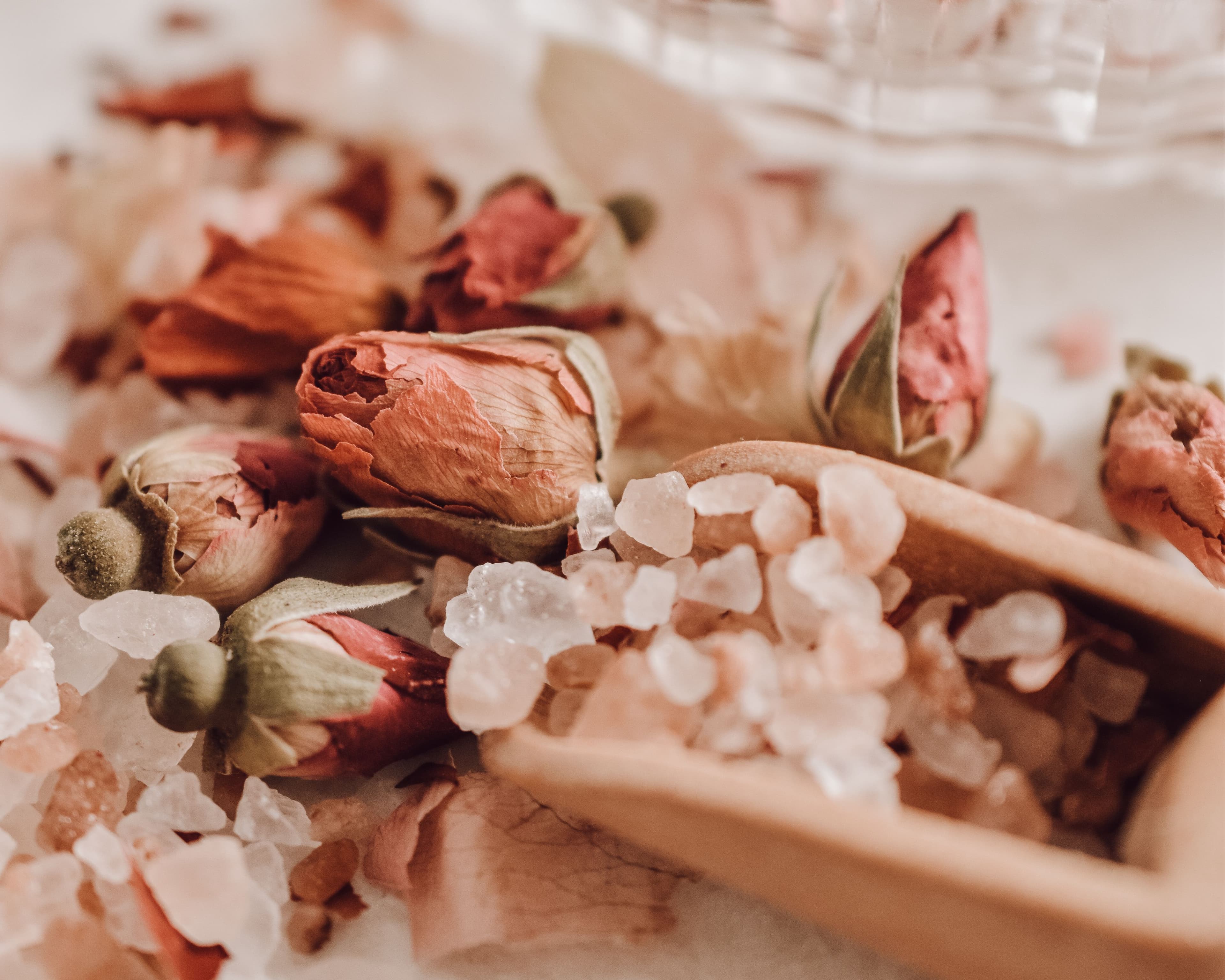 Dried rose buds and pink salt in a wooden scoop